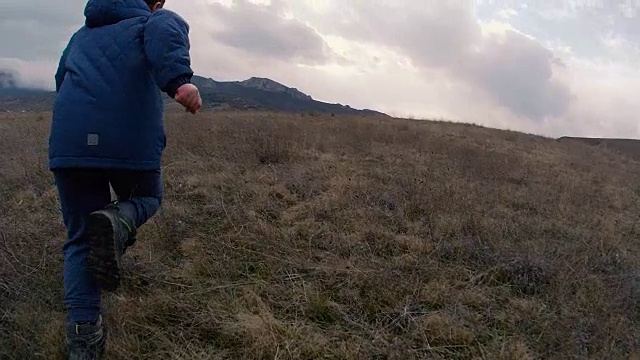 一个小男孩在山坡上跑到雾气弥漫的山上。慢动作视频
