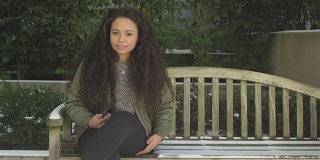 一位美丽的年轻女子耐心地坐在木凳上。然后她把手机收起来