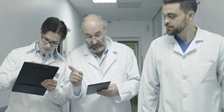 三名男医生走在医院走廊上讨论病人的笔记。FullHD