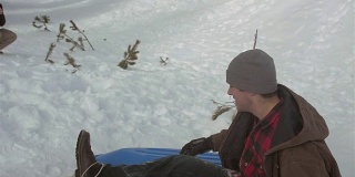 一个年轻人从雪山上滑下来的慢动作镜头。然后他在空中短暂飞行，然后突然着陆