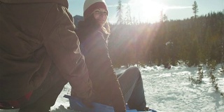 年轻美丽的女人看着镜头，微笑着坐在她的雪橇上。镜片耀斑