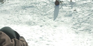 在她的肩膀上，一个年轻的男人推着他的女朋友，她正骑着雪橇从雪山上滑下来。在慢动作