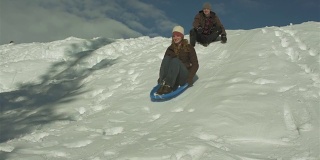 一名年轻男子推着他的女朋友坐着雪橇从雪山上滑下来。在慢动作