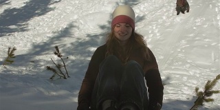 一名年轻男子推着他的女朋友坐着雪橇从雪山上滑下来。在慢动作