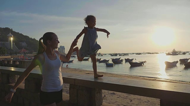 年轻的母亲带着小女儿在海边慢镜头奔跑。