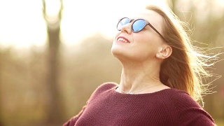 一位美丽的三十岁戴眼镜的女人把她的脸对着春天的太阳。他把手摆好，迎着风走了过去。与自然统一。享受春暖花开视频素材模板下载