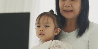 现代生活的泰国母亲和她的女儿正在看卡通在他们的卧室笔记本电脑上的休闲活动-母亲和她的宝宝的亲戚与母亲节的概念