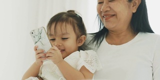泰国的现代生活，妈妈和她的女儿在他们的卧室用智能手机拍照和看卡通休闲活动-母亲和她的宝宝的亲戚与母亲节的概念