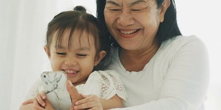 泰国的现代生活，妈妈和她的女儿在他们的卧室用智能手机拍照和看卡通休闲活动-母亲和她的宝宝的亲戚与母亲节的概念