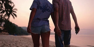 浪漫的情侣在迷人的夕阳下手牵着手漫步在沙滩上。幸福的年轻夫妇在旅游假期享受海洋日落。缓慢的运动。1920 x1080