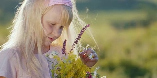 可爱的小女孩享受着大自然，看着一束野花