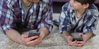 儿子和父亲躺在地板上玩智能手机，缺乏关爱