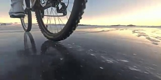 看轮胎。60 fps actioncam开枪。一个女人在冰上骑自行车。结冰的贝加尔湖的冰。自行车的轮胎上覆盖着特殊的尖钉。