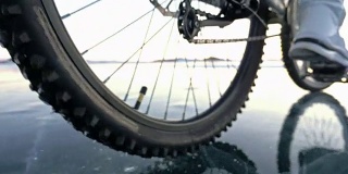 看轮胎。180 fps射击。一个女人在冰上骑自行车。结冰的贝加尔湖的冰。自行车的轮胎上覆盖着特殊的尖钉。