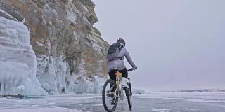 一个女人在冰洞附近骑自行车。有冰洞和冰柱的岩石非常漂亮。这个女孩穿着银色的羽绒服，背着自行车背包，戴着头盔。旅行者正在骑自行车。