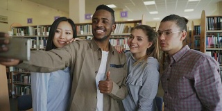 一群留学生在大学图书馆用智能手机自拍，开心地微笑着。快乐的朋友们在一起准备项目的同时休息
