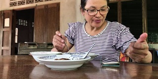 亚洲女性使用智能手机，在家吃午饭