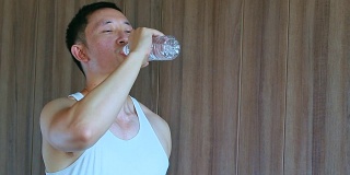 亚洲男人在去健身房后喝水，干渴和运动后疲惫