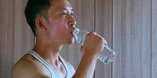 亚洲男人在去健身房后喝水，干渴和运动后疲惫