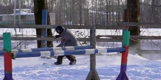 慢镜头:一个女孩骑着马疾驰。一匹马用绳子拖着一个滑雪者。滑雪者在雪堆中骑在滑雪板上。女骑师和男滑雪板运动员通过跳板进行跳跃