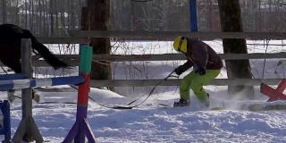 慢镜头:一个女孩骑着马疾驰。一匹马用绳子拖着一个滑雪者。滑雪者在雪堆中骑在滑雪板上。女骑师和男滑雪板运动员通过跳板进行跳跃