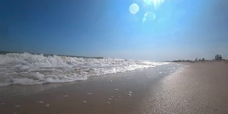 在一个阳光明媚的夏日，在美丽的沙滩上，海浪盖住了相机。从低角度，慢动作拍摄动作摄像机。