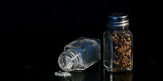 海盐和黑胡椒在玻璃罐中展示在黑色的背景