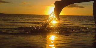 特写:无忧无虑的女人在金色的夕阳下赤脚在浅海中奔跑。