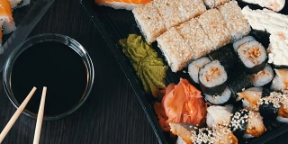 在时尚的黑色背景上，配有各种寿司卷、寿司卷、手握寿司、粗看寿司。酱油和竹筷就在旁边