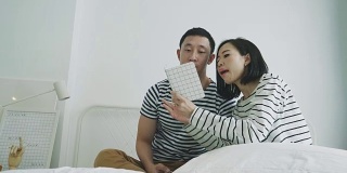 一个泰国女人在她的男朋友旁边写卡片，同时使用智能手机，她想分享她的卡片给她的男朋友和一起讨论-周末的休闲活动