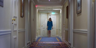 穿着蓝色裙子的漂亮女人走在豪华大厦的走廊上