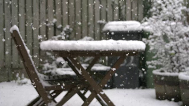 英国的一个花园正在下雪，花园里有家具和有轮子的垃圾桶