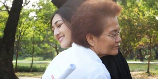 年轻的亚洲女学生戴着毕业帽和毕业礼服在大学，女性与毕业概念。怀着快乐的心情拥抱母亲的女人。