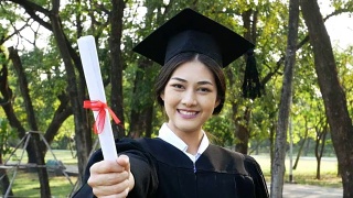 年轻的亚洲女学生戴着毕业帽和礼服，花园背景，女性与毕业概念。视频素材模板下载
