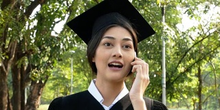 年轻的亚洲女性学生使用智能手机与朋友在公园，花园背景，女性与毕业概念。