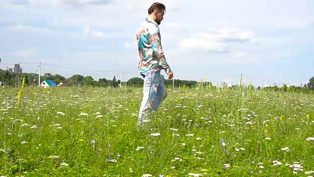 一个穿着破洞牛仔裤的英俊男子独自在草地上走来走去。