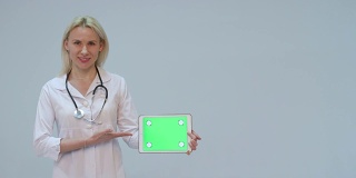 一个女医生的肖像与白色大衣和平板与绿色屏幕和听诊器微笑
