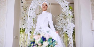 美丽的新娘在白色传统穆斯林礼服与一束鲜花