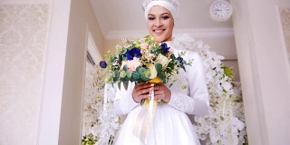 美丽的穆斯林新娘与化妆在白色婚纱来到鲜花