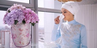 年轻的穆斯林新娘在蓝色婚纱喝一杯咖啡
