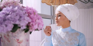 美丽的穆斯林模特在蓝色婚纱喝咖啡