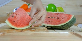 近距离拍摄的女人的手用菜刀切熟西瓜木板上的夏天新鲜水果