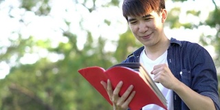 英俊的学生站在那里，手里拿着红皮书。男性的快乐的生活方式。教育的概念。