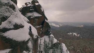 一个攀岩者在一个阳光明媚的冬日攀登陡峭悬崖的鸟瞰图。视频素材模板下载