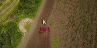 无人机跟踪拍摄拖拉机播种，在田间播种农作物。从上面的观点