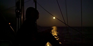 4K女人在帆船上放松，背景是满月照在海上