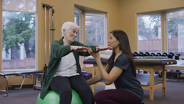 坐在健身球上的老年妇女在物理治疗