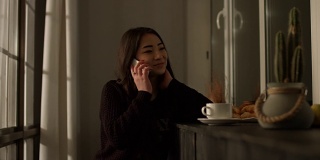 漂亮的亚洲女孩在家里用智能手机聊天