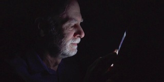 一位老人深夜在家用手机看新闻。只照亮黑暗的脸