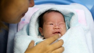 在医院的产房里，年轻的母亲抱着她刚出生的亚洲宝宝哭泣视频素材模板下载